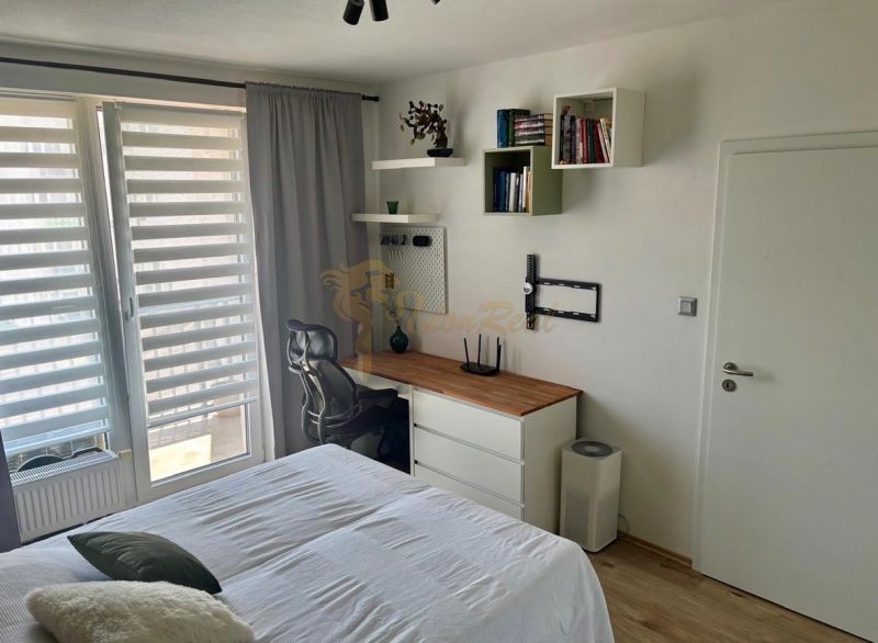 Bedroom in a 2-room apartment with a work corner, bed, and wooden decor on the floor.
