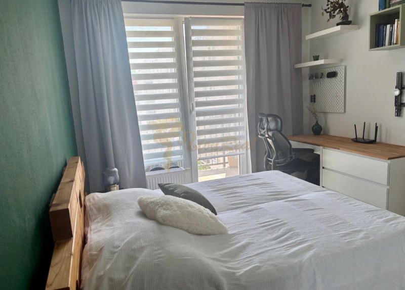 Bedroom in a 2-room apartment with a desk and large windows.