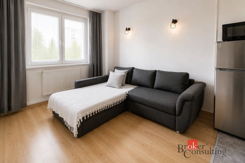 Living room in a two-room apartment with a sofa, wooden decor flooring, and a refrigerator.