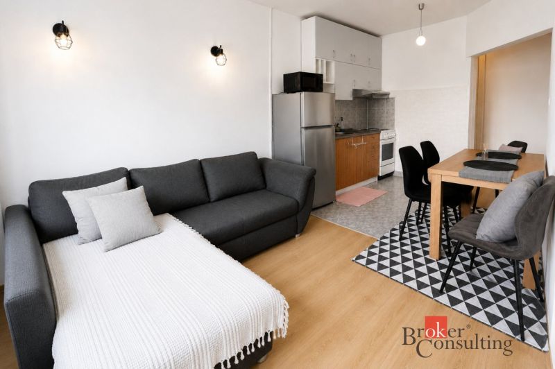 Stylish interior of a 2-room apartment with wood-patterned flooring, a kitchen, and a dining table.