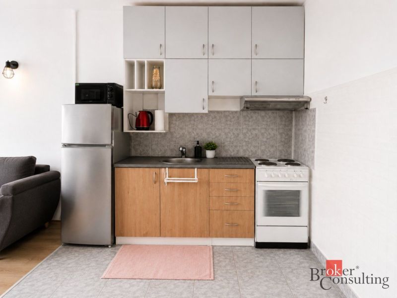 A kitchen in a 2-room apartment with appliances and a wooden decor floor.