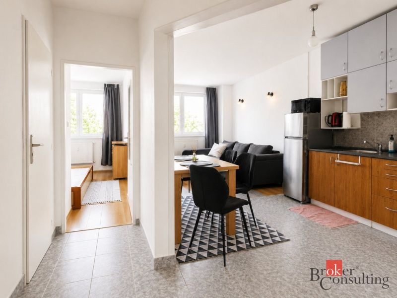 Interior of a 2-room apartment with a kitchen, dining table, and wooden decor flooring.