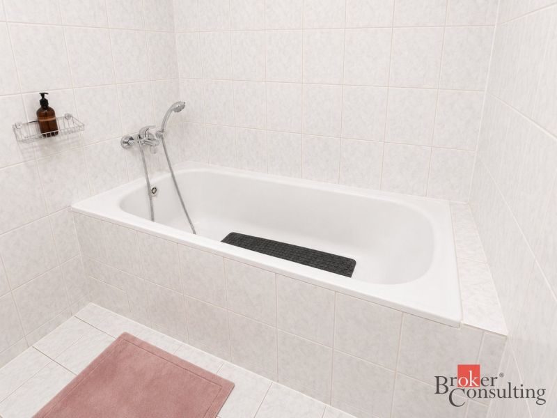 A bathroom with a bathtub tiled with white tiles in a 2-room apartment.