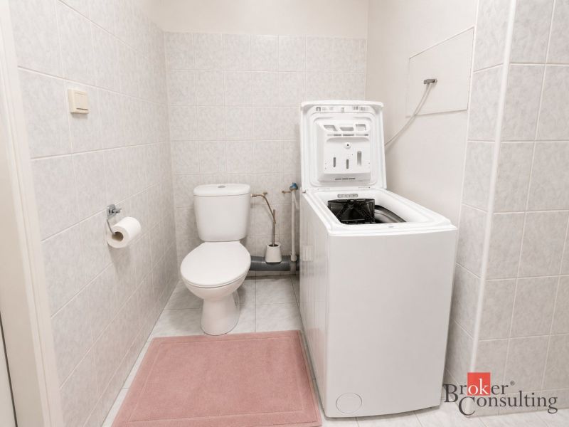 Bathroom in a 2-room apartment with a washing machine and toilet on the tiles.
