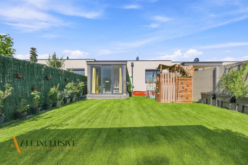 A garden of a family house in Oľdza with a lawn, a children's playground, and plants in pots.