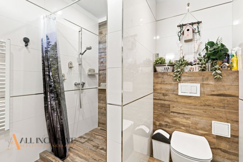 A bathroom in a family house with a wooden decor floor and a shower with a curtain.