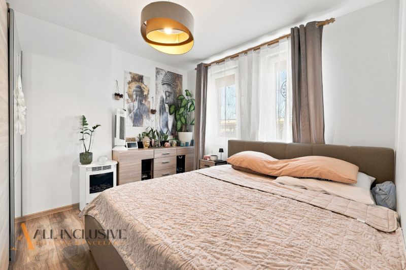 Bedroom with light walls, a bed, and decorations, floor with wooden decor.