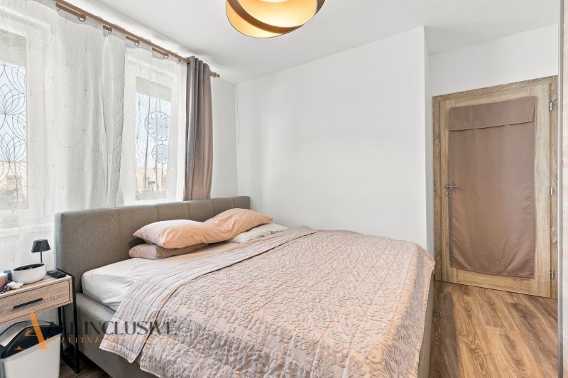 A bedroom in a family house with a wooden decor floor, a gray bed, and curtains.