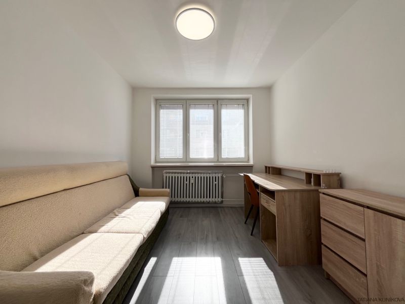 A room in a 3-room apartment with a sofa, a desk, and a wooden decor floor.