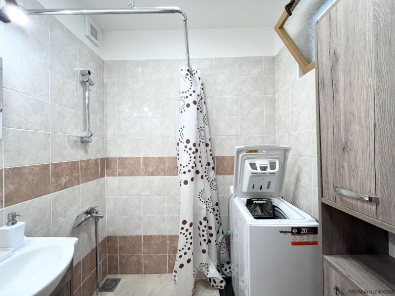 A bathroom in a 3-room apartment with a washing machine, a sink, and a shower with a curtain.