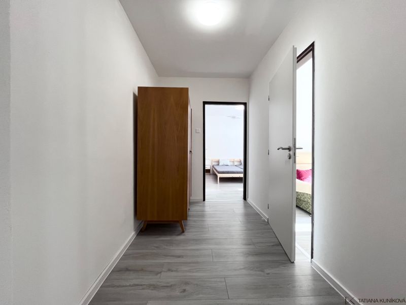 A hallway with a wooden decor floor in a 3-room apartment, a dark wardrobe, doors to the rooms.