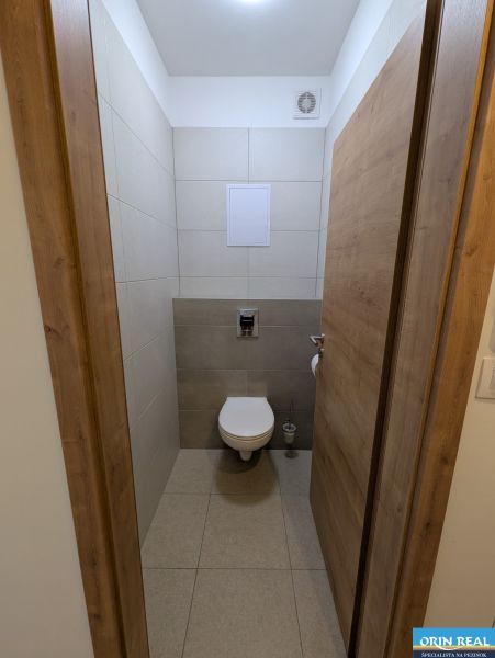 A toilet in a 2-room apartment with ceramic tiles and a wooden decor floor.