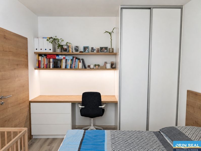 A bedroom in a two-room apartment with a work corner, books, and a floor with a wooden decor.