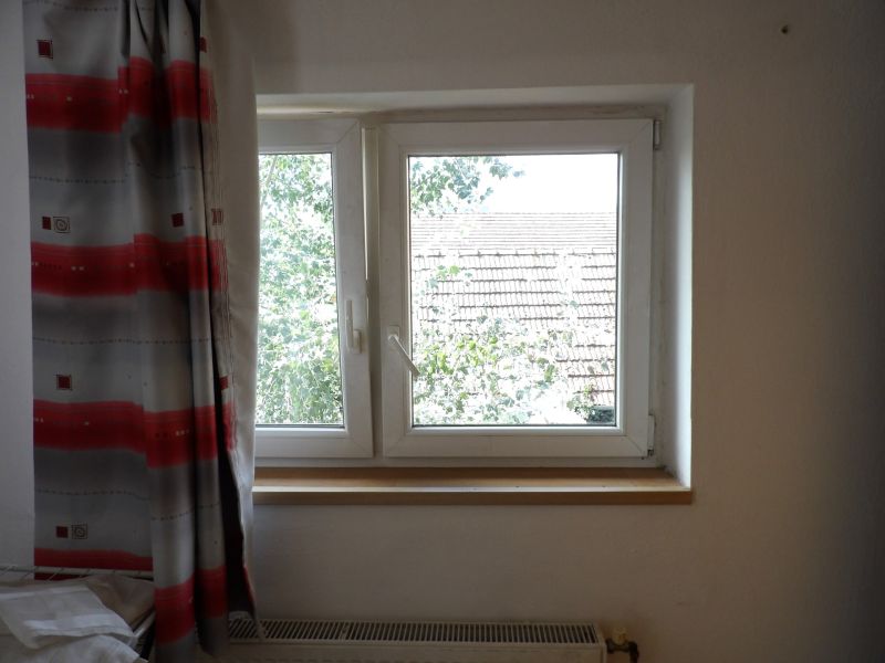 A window with a curtain and a view of the roof in a 2-room apartment.