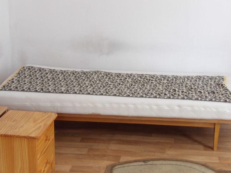 A bed in a room with a wood-patterned floor, next to a wooden cabinet.