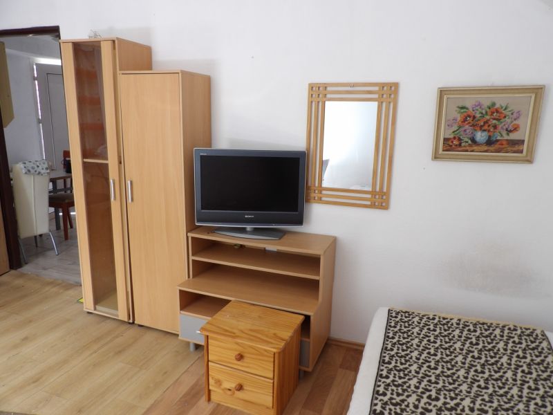 A television on a low cabinet, a wardrobe, and a mirror in a 2-room apartment with a wooden decor floor.