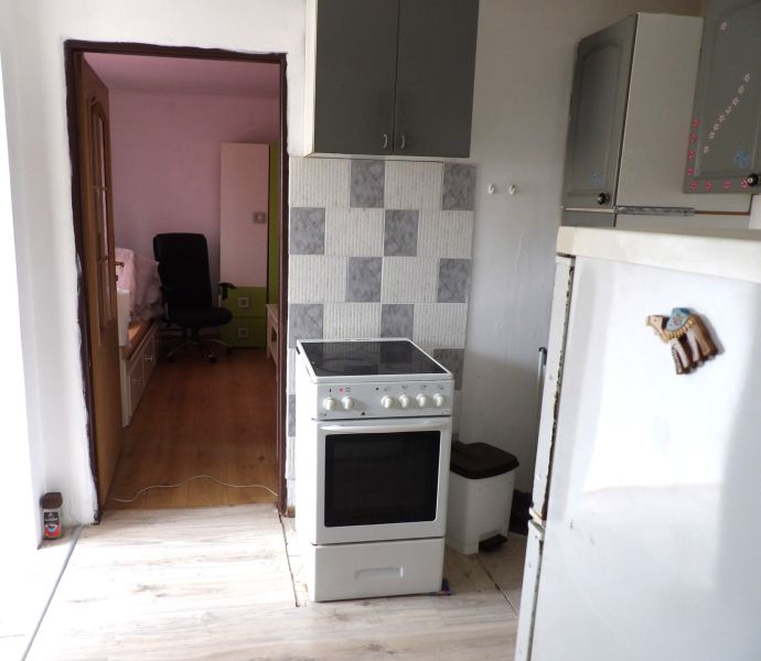 A kitchen in a 2-room apartment, overlooking the living room with a wooden decor floor.