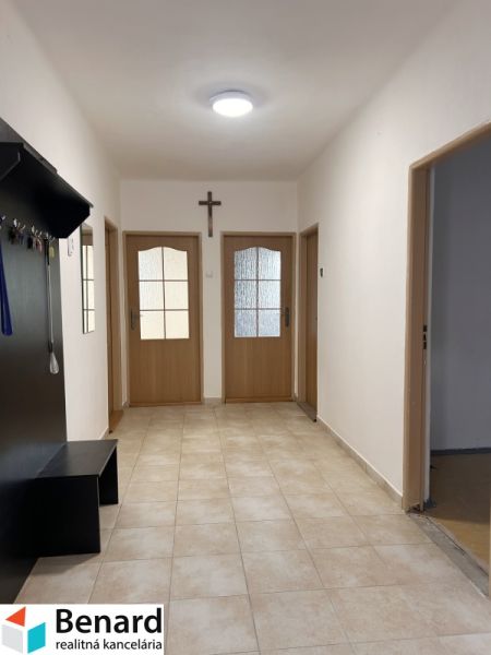 A hallway in a family house with tiles, wooden doors, and a coat rack.