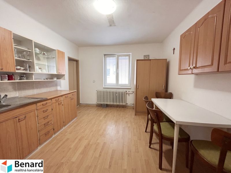 A kitchen in a family house with a wooden decor floor, wooden cabinets, and a dining table.