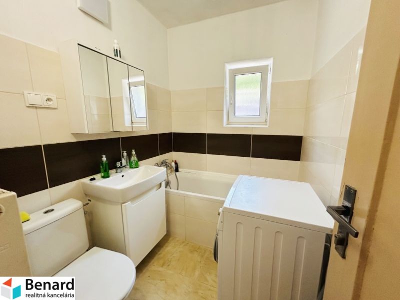 A bathroom in a family house with a bathtub, a washing machine, and a sink, with light tiles.