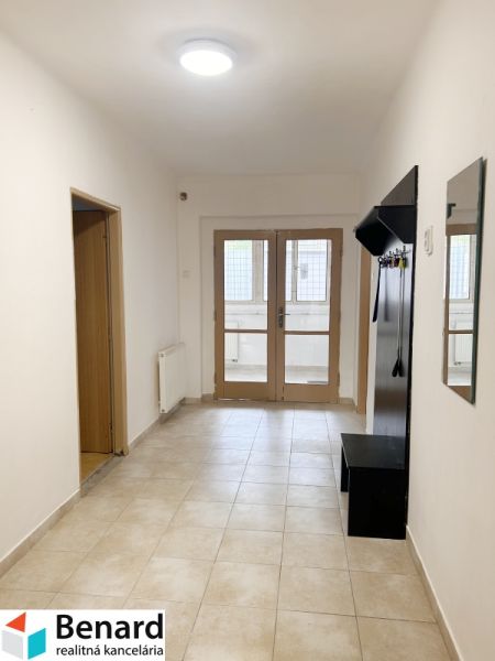 A hallway with a coat rack and tiles in a family house, the door leads to a glassed-in terrace.
