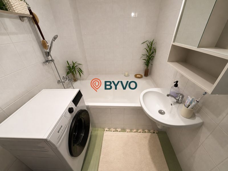 A bathroom in a 2-room apartment with a bathtub, sink, and washing machine. Neutral shades.