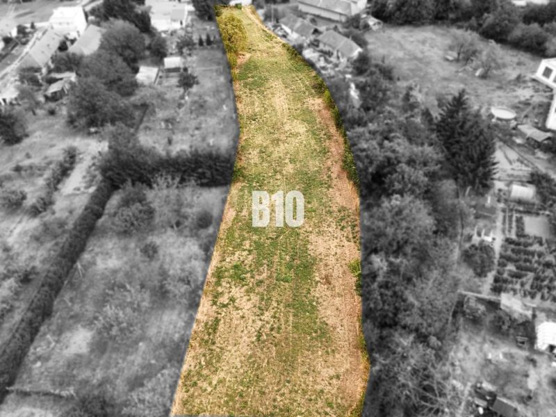 Plots - housing Kolíňany: Long plot with green grass, lined with trees and buildings.