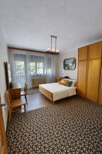 A bedroom in a family house with carpet flooring, a bed, and wooden furniture.