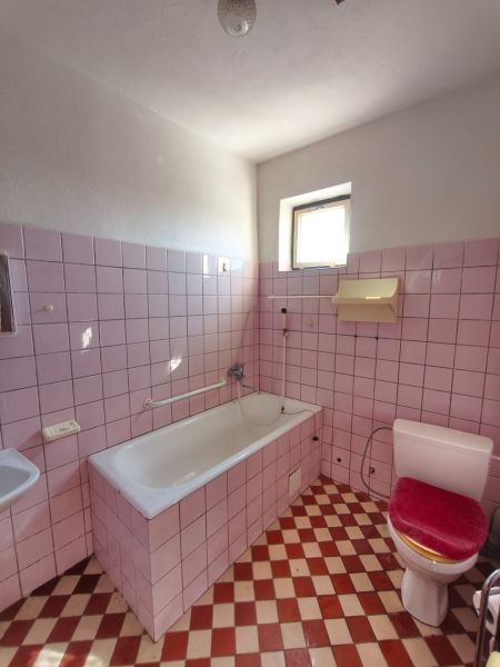 A bathroom with pink tiles and a white bathtub in a family house.