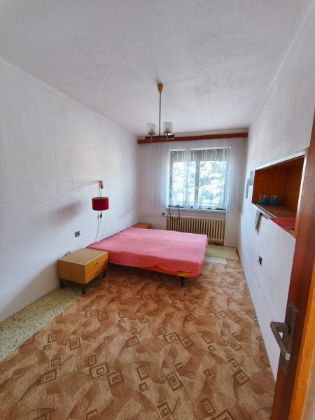 Bedroom in a family house with a bed, carpet, and a window with a white curtain.