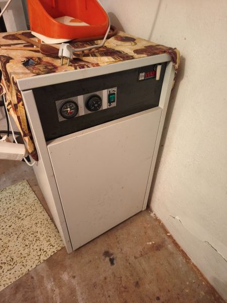 A boiler in the interior of a family house with a control panel and an orange container on top.