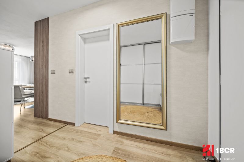 In the 2-room apartment, there is a mirror with a golden frame and a floor with a wooden decor.