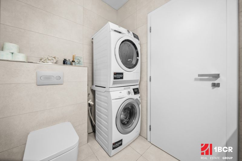 Washer-dryer in the bathroom of a 2-room apartment, light tiles and toilet.