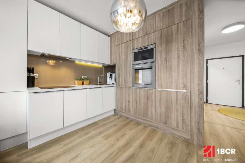 A kitchen in a 2-room apartment, white cabinets, wooden decor flooring, built-in appliances.