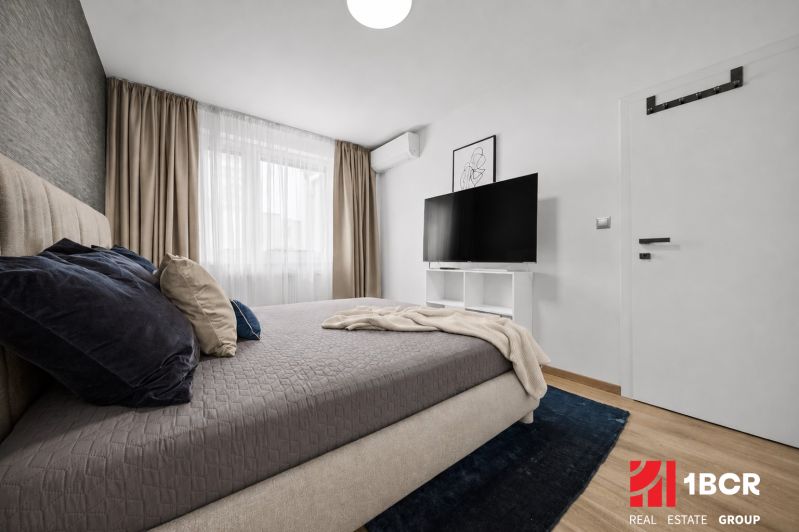 Bedroom with a bed, television, and wood-decor flooring in a 2-room apartment.