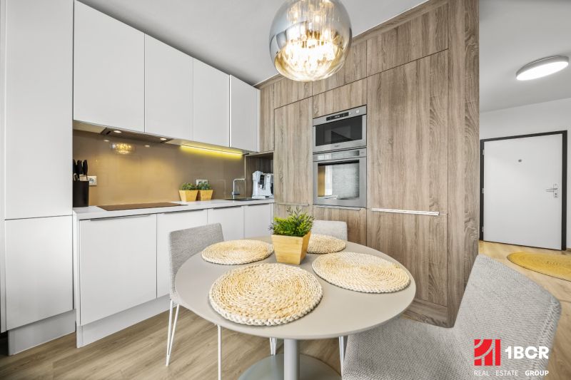 A kitchen in a 2-room apartment with a wood-patterned floor, a table, and built-in appliances.