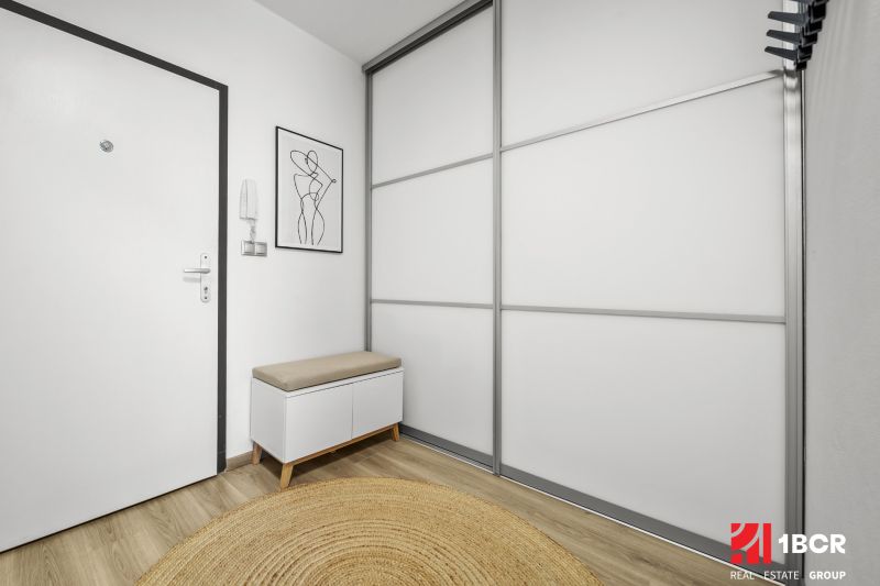 Entrance hall in a 2-room apartment with wood-patterned flooring and minimalist furniture.