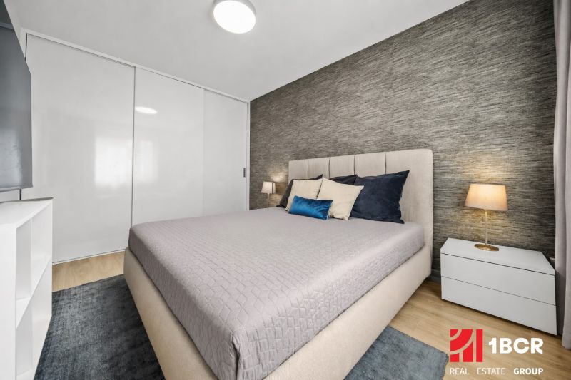 A bedroom in a 2-room apartment with a bed, nightstands, and a floor with a wooden decor.