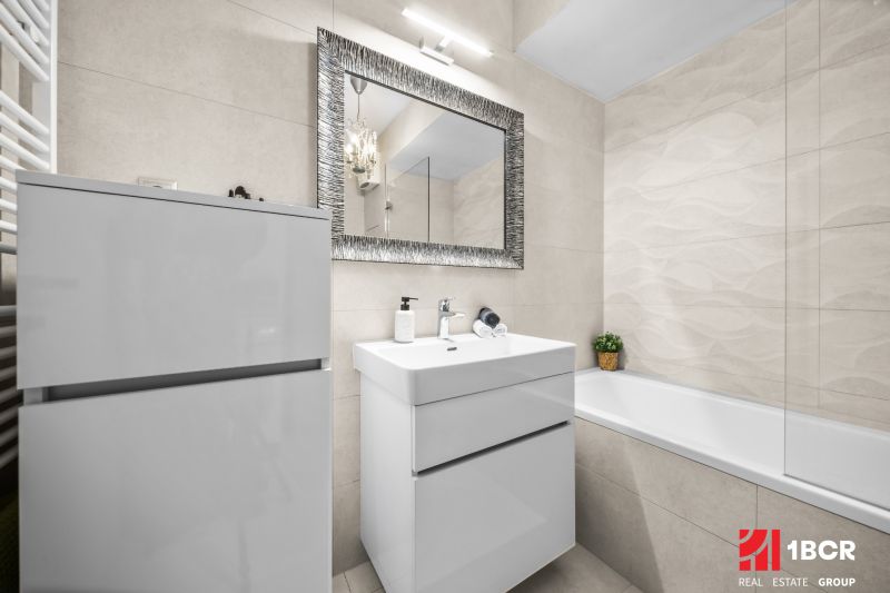 A bathroom with a mirror, sink, and bathtub in a 2-room apartment; clean and bright design.