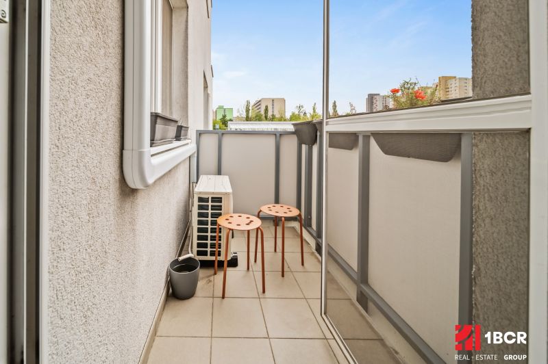 A balcony with two orange chairs in a 2-room apartment with a view of the city.