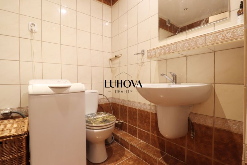 Bathroom in a 2-room apartment with a washing machine and toilet, tiles with a subtle pattern.