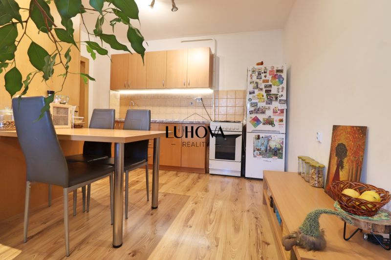 A kitchen in a 2-room apartment with a wooden decor floor, a dining table, and a refrigerator.