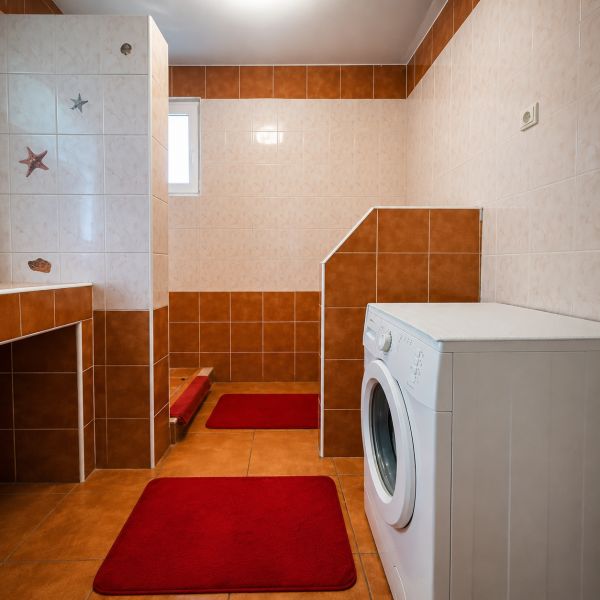 Bathroom in a family house with a shower and a washing machine, tiles in shades of brown.