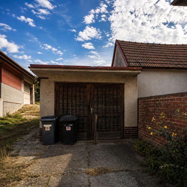 A family house with a garage in Šalgočka, with two trash bins and a brick wall.
