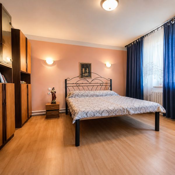 Bedroom with a metal bed, wooden decor flooring, furniture, and curtains in a family house.