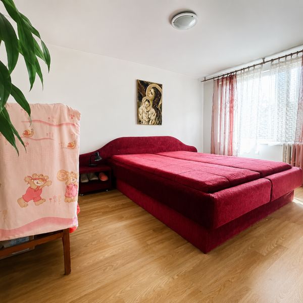 A bedroom in a family house with a red bed and a wooden decor floor.