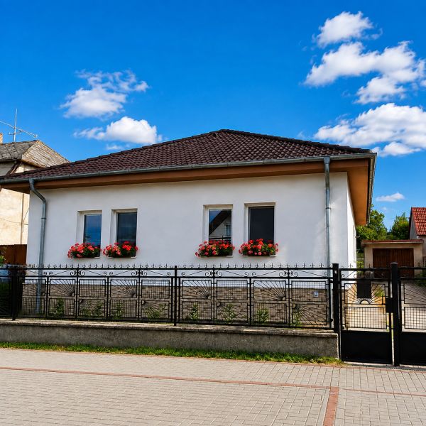 A family house in Šalgočka with a white facade, window flowers, and a hipped roof.