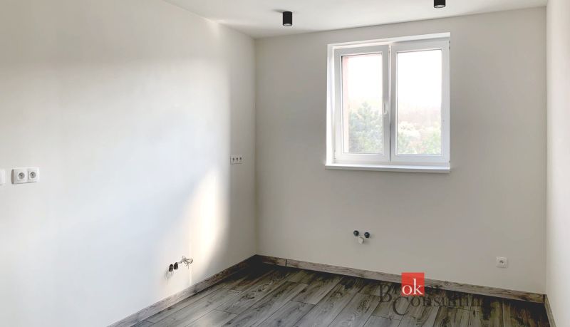 A simple room in a one-bedroom apartment with a wooden-patterned floor and white walls.