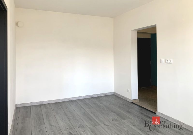 An empty room in a one-room apartment with a wood-patterned floor.