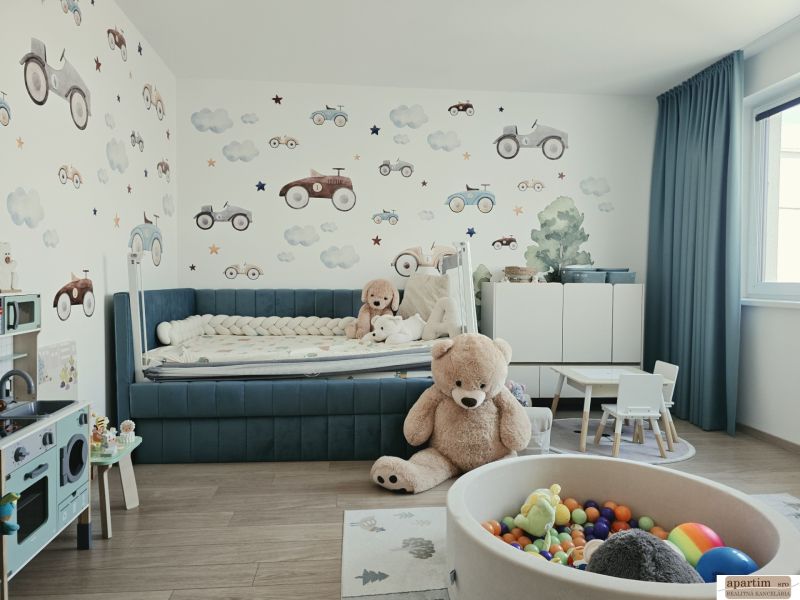 Children's room with toys, a blue bed, wallpaper with cars, and a wooden decor floor.
